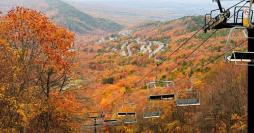A scenic view of a chairlift overlooking a vibrant autumn landscape with colorful trees and winding roads.