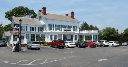 A McDonald's restaurant in a large, historic white building with a parking lot filled with cars on a sunny day.