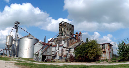 Abandoned industrial building with silos and rusted structures under a cloudy sky.