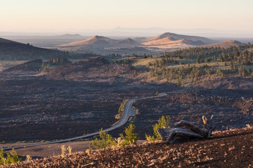 A winding road through a rugged landscape of volcanic rock and rolling hills under a soft morning light.