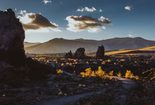 A scenic landscape featuring rocky formations, mountains, and golden foliage under a dramatic sky at sunset.