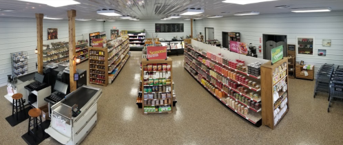 A spacious store interior with shelves of products, a checkout area, and seating, featuring organized displays and bright lighting.