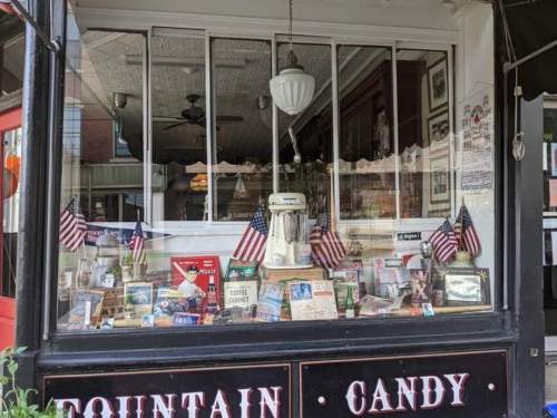 A vintage candy shop window displays memorabilia, books, and small American flags, creating a nostalgic atmosphere.