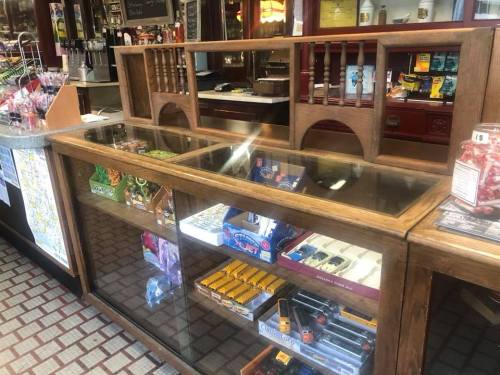 A wooden counter with a glass display showcasing various items, including snacks and tobacco products.