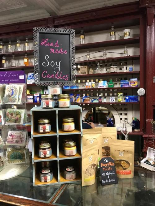 Display of handmade soy candles and local treats in a shop, with a chalkboard sign highlighting the products.
