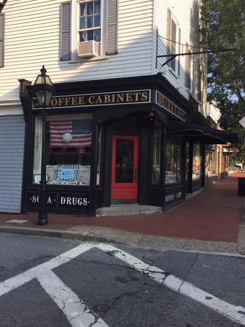 A corner store with a sign reading "Coffee Cabinets," featuring an American flag and a classic streetlamp outside.
