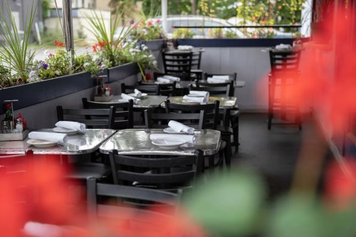 A cozy restaurant patio with empty tables set for dining, surrounded by vibrant flowers.