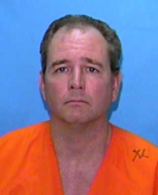 Mugshot of a man in an orange prison jumpsuit against a blue background, looking directly at the camera.