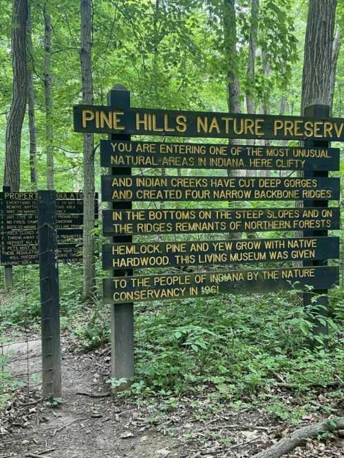 Sign at Pine Hills Nature Preserve, detailing natural features and history of the area, surrounded by lush green trees.