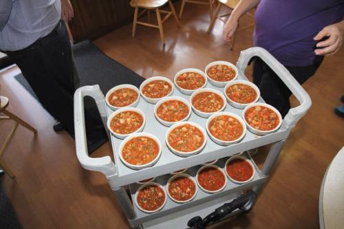 A cart with 15 bowls of soup, each filled with a hearty tomato-based mixture, being served in a dining area.