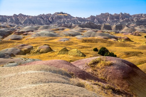 Vibrant, rolling hills in a colorful landscape with rugged mountains in the background under a clear blue sky.