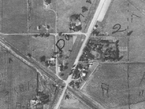 Aerial view of a rural area with intersecting roads, houses, and fields, marked with letters and numbers.