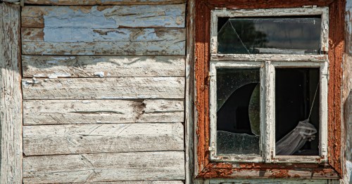 a rustic window with peeling red paint and shattered glass panes on a white-washed wooden wall.