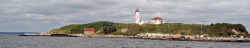A scenic view of a lighthouse on a green hill by the water, with rocky shores and a cloudy sky in the background.