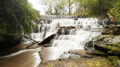 A serene waterfall cascading over rocky steps, surrounded by lush greenery and trees.