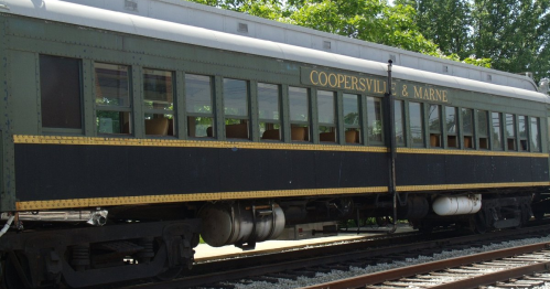 A vintage train car labeled "Coopersville & Marne" parked on the tracks, surrounded by greenery.