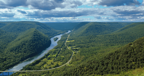 A scenic view of rolling green hills and a winding river under a partly cloudy sky.