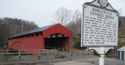A red covered bridge with a historical marker nearby, set against a hilly landscape.