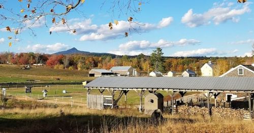 A scenic farm landscape with barns, fields, and colorful autumn trees under a blue sky with fluffy clouds.