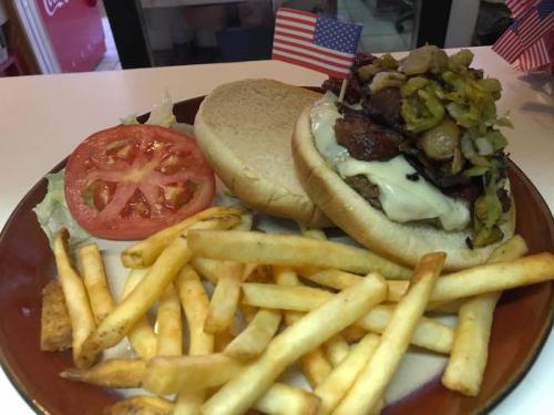 A plate with a burger topped with vegetables, a slice of tomato, and a side of golden French fries.