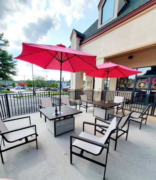 Outdoor patio with pink umbrellas, tables, and chairs, set against a clear sky and nearby parking lot.