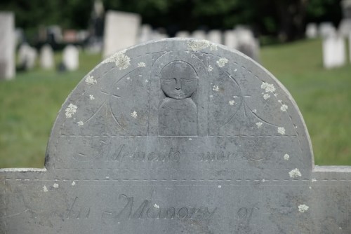 A weathered gravestone with an engraved face and the inscription "In Memory of" partially visible.
