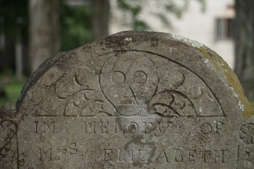Close-up of an old gravestone with a skull and floral design, inscribed "In memory of Mrs. Elizabeth."