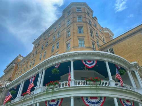 Historic building with a curved porch, decorated with red, white, and blue bunting and American flags under a blue sky.