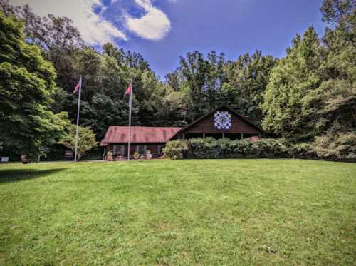 A rustic building with a red roof, surrounded by trees and a green lawn, featuring decorative flags and a quilt pattern.