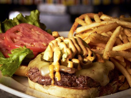 A juicy cheeseburger topped with lettuce, tomato, pickles, and sauce, served with a side of crispy French fries.