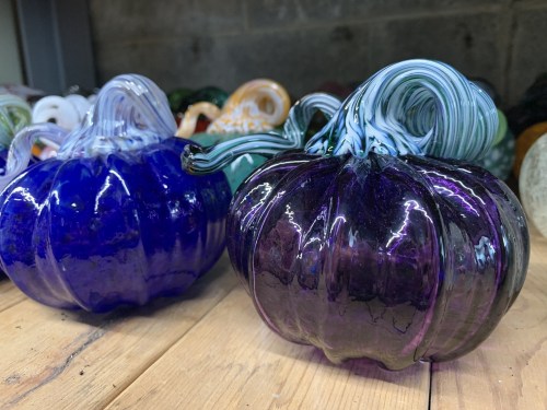 Two glass pumpkins, one blue and one purple, with intricate swirled stems, resting on a wooden surface.