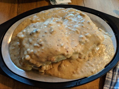 A plate of biscuits smothered in creamy sausage gravy, served on a black dish.