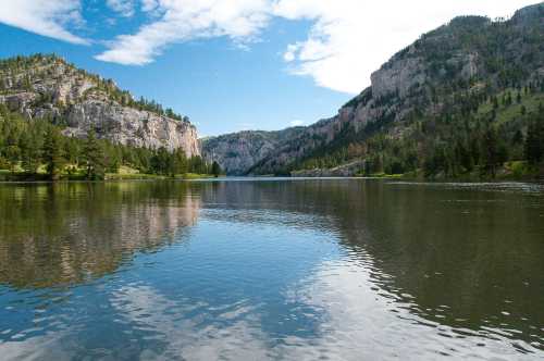 A serene lake surrounded by mountains and trees, reflecting the sky and landscape in calm waters.