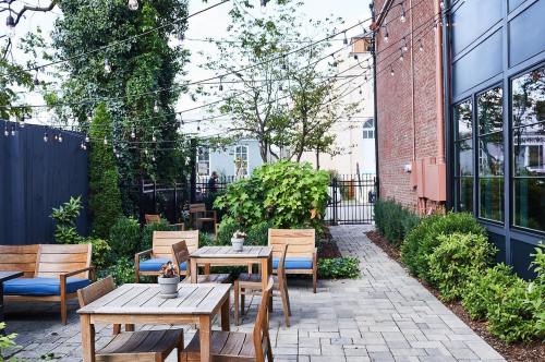 A cozy outdoor patio with wooden tables and chairs, surrounded by greenery and string lights overhead.