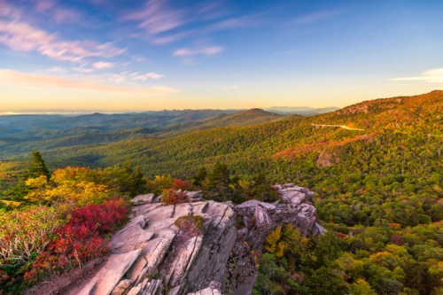 A scenic view of colorful autumn foliage on mountains under a vibrant sky at sunset.