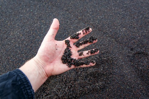 A hand with black sand resting on a dark surface, showcasing the texture and grains of the sand.