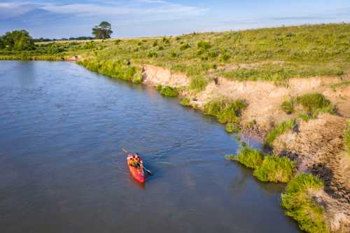 A person kayaking on a calm river surrounded by lush green banks and a clear blue sky.