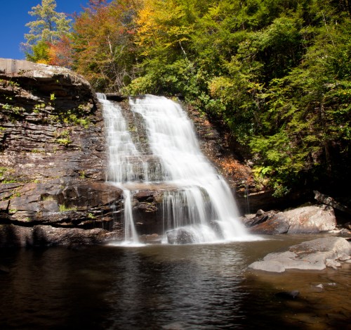 A serene waterfall cascading over rocky cliffs, surrounded by vibrant autumn foliage and a calm pool below.