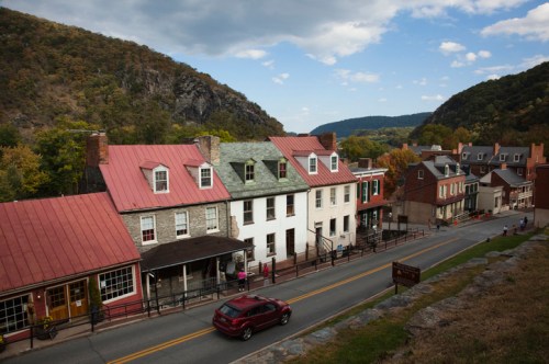 Historic buildings line a street in a valley, surrounded by hills under a partly cloudy sky.