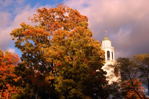 A vibrant autumn scene featuring colorful trees and a historic building under a dramatic sky.