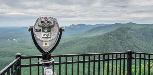 A scenic view of mountains from a lookout point, featuring a coin-operated binocular viewer in the foreground.