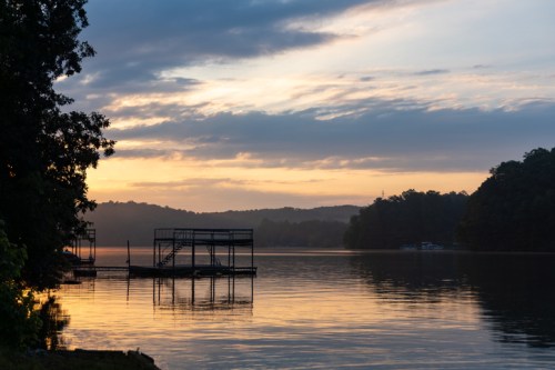Sunrise over a calm lake, with silhouettes of docks and trees against a colorful sky.