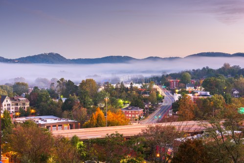 A scenic view of a misty valley at dawn, with mountains in the background and a quiet road lined with trees.