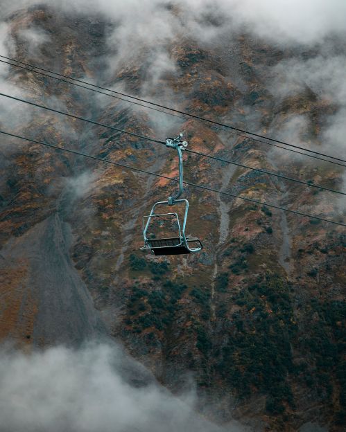 A lone ski lift chair suspended above a misty mountain landscape.
