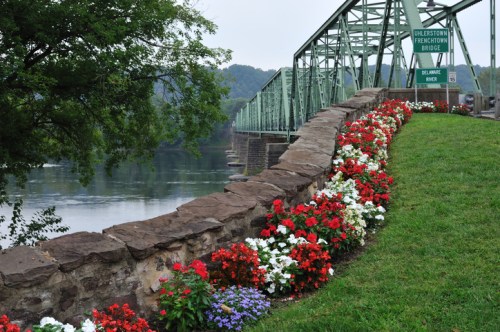 A scenic view of a green bridge over a river, surrounded by colorful flower beds and lush greenery.