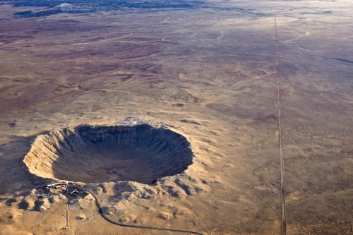 Aerial view of a large crater surrounded by barren land, with a road stretching into the distance.