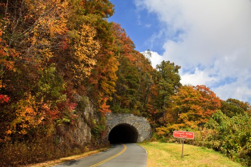 A scenic road leads to a stone tunnel, surrounded by vibrant autumn foliage and a sign for "Hawkins Village."