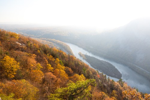 A scenic view of a winding river surrounded by vibrant autumn foliage and misty mountains in the background.