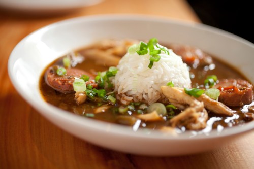 A bowl of gumbo with chicken, sausage, and a mound of white rice, garnished with green onions.