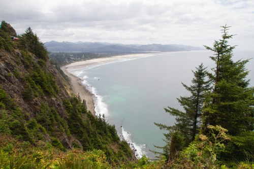 A scenic coastal view with cliffs, lush trees, and a sandy beach under a cloudy sky.